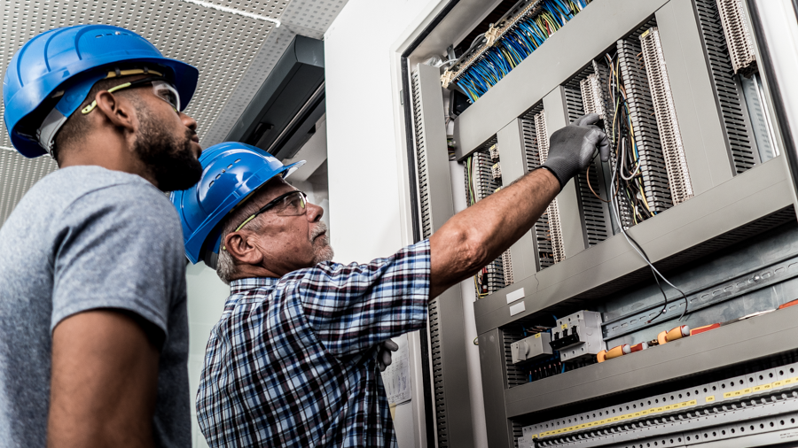 Jüngerer Elektriker schaut älterem beim arbeiten zu